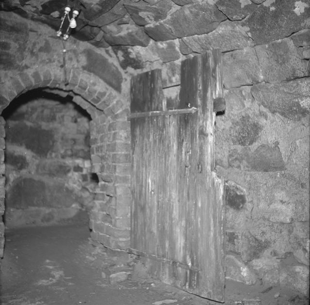 Kuva: Köyliön kartanon kellarin ovi. Ovi kuvan keskellä, vasemmalla holvikaaren muotoinen oviaukko. Kiviseinät ja maalattia. Satakunnan Museo. CC BY 4.0 Raimo Seppälä 1956