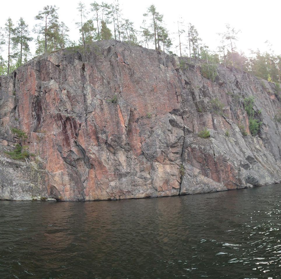 Mäntyharju, Haukkavuori. Kalliomaalauskohteen laajin kuvakenttä (Haukkavuori I) sijaitsee jylhässä veteen tippuvassa kalliossa. Maalaukset sijaitsevat noin 1,5 metriä vedenpinnan yläpuolella, noin viiden metrin levyisenä vyöhykkeenä (pääosin kuvan vasemmassa puoliskossa). Kuvattu kohti itää. Teemu Mökkönen 29.7.2021