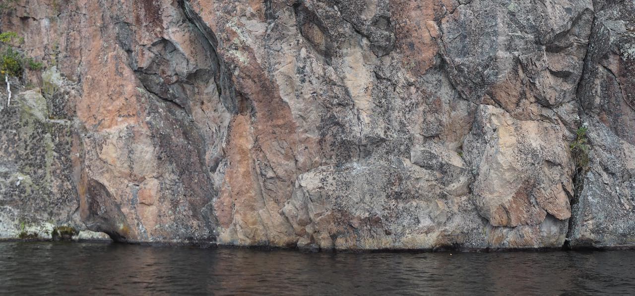 Mäntyharju, Haukkavuori. Kalliomaalauskohteen laajin kuvakenttä (Haukkavuori I), jossa heikosti erottuvat maalaukset sijaitsevat kolmena ryhmänä noin 1,5 metriä vedenpinnan yläpuolella. Vasemmalla käsi, keskellä ihminen pää alaspäin ja oikealla heikosti erottuva verkkokuvio. Teemu Mökkönen 29.7.2021